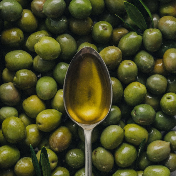 Spoon with olive oil surrounded by green olives on a dark background